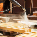 Application of flame retardant to ensure fire protection, airless spraying device. Woodworker clean the plank from shavings in workshop. Carpenter coating cuttings from wooden bar.